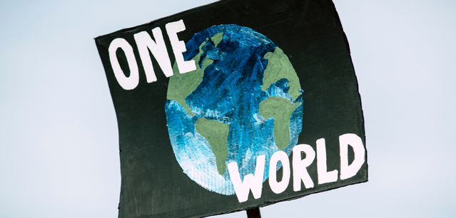 A protest sign with a painted globe and the words ONE WORLD written in white letters against a light blue sky.