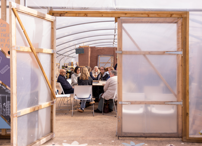 An open door looking into a space at Civic Square that has groups of people sat around tables having a discussion
